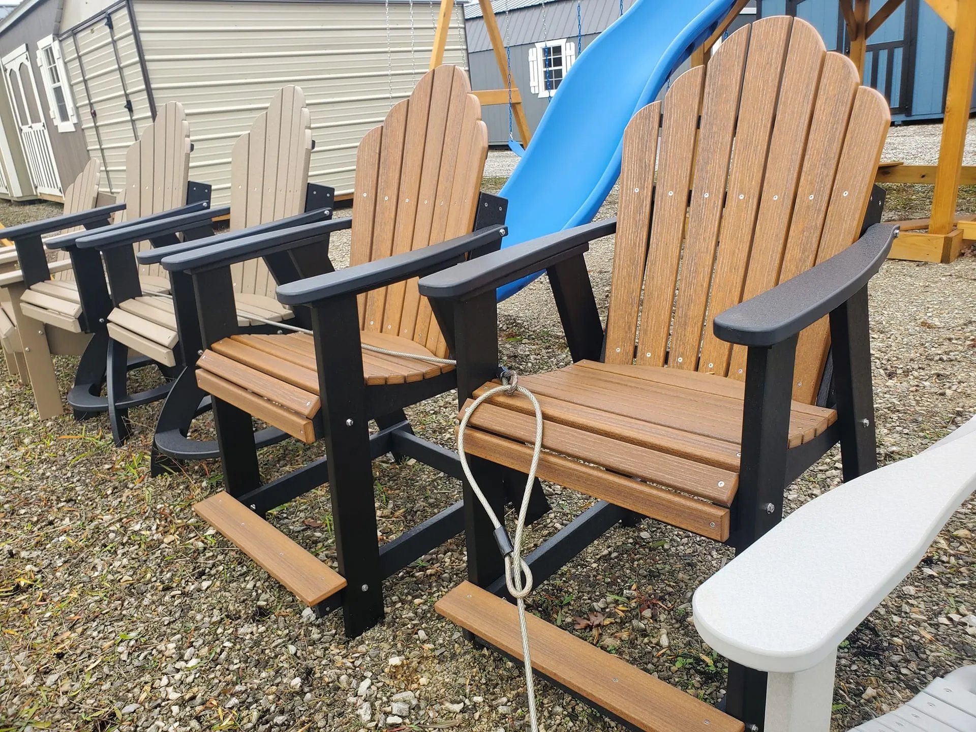 Wooden Adirondack chairs with black frames near a blue playground slide